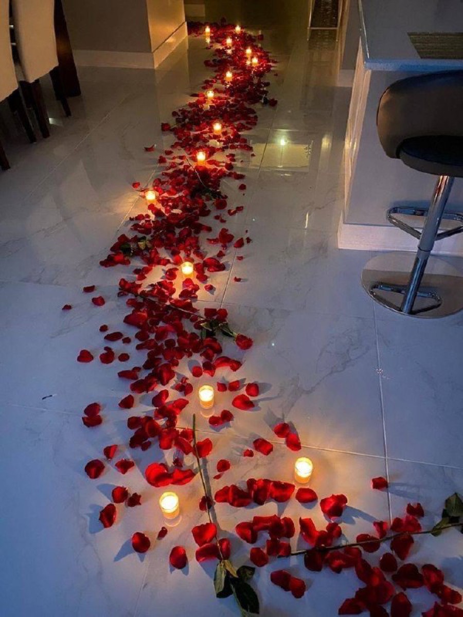 Pétalas de rosas vermelhas espalhadas com velas acesas em ambiente romântico